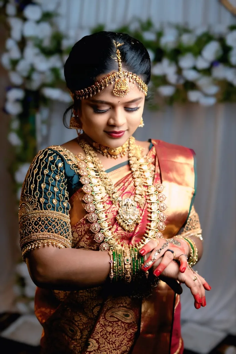 South Indian bride in red and green wedding attire looking down at her mehendi