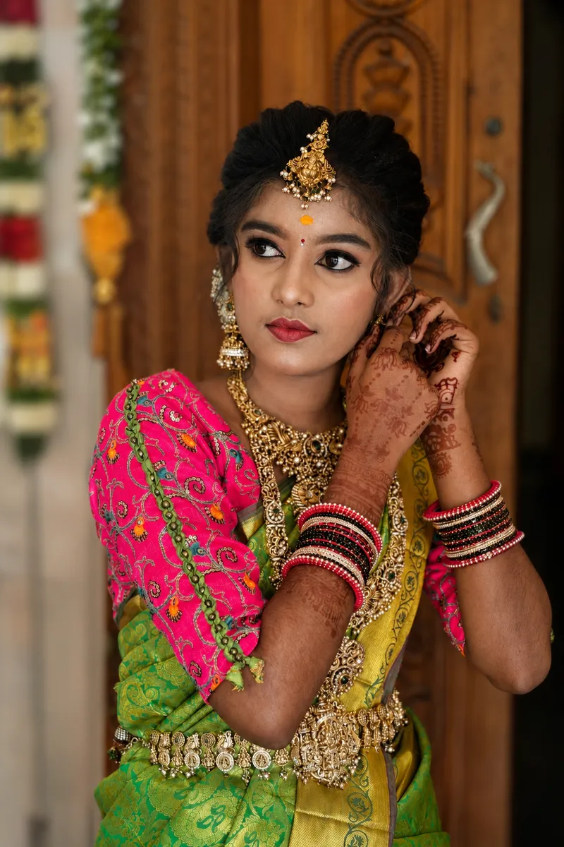 Bride adjusting her earring in bright pink and green wedding attire